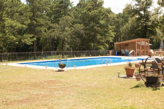In-ground pool with blue water and pergola under the pines